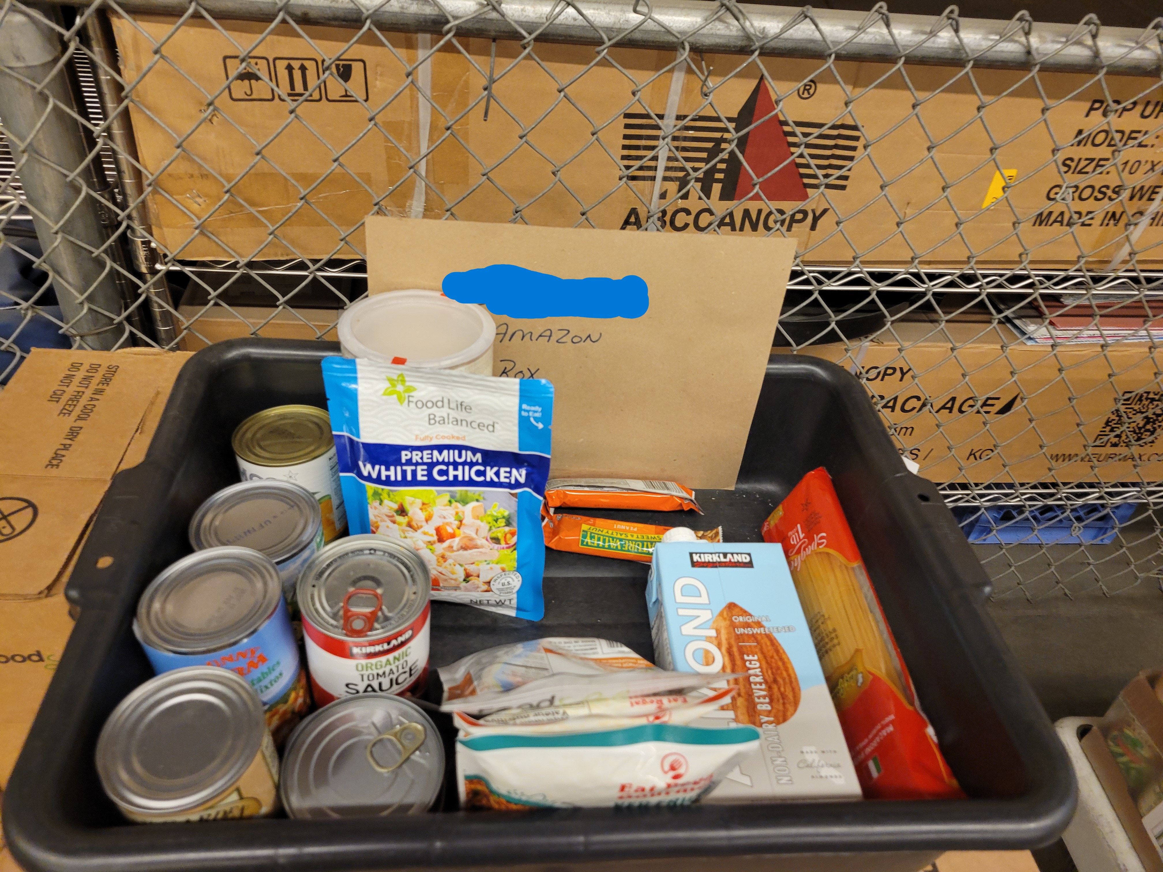 Tub of dry goods with a sign listing amazon box on top of cardboard boxes.